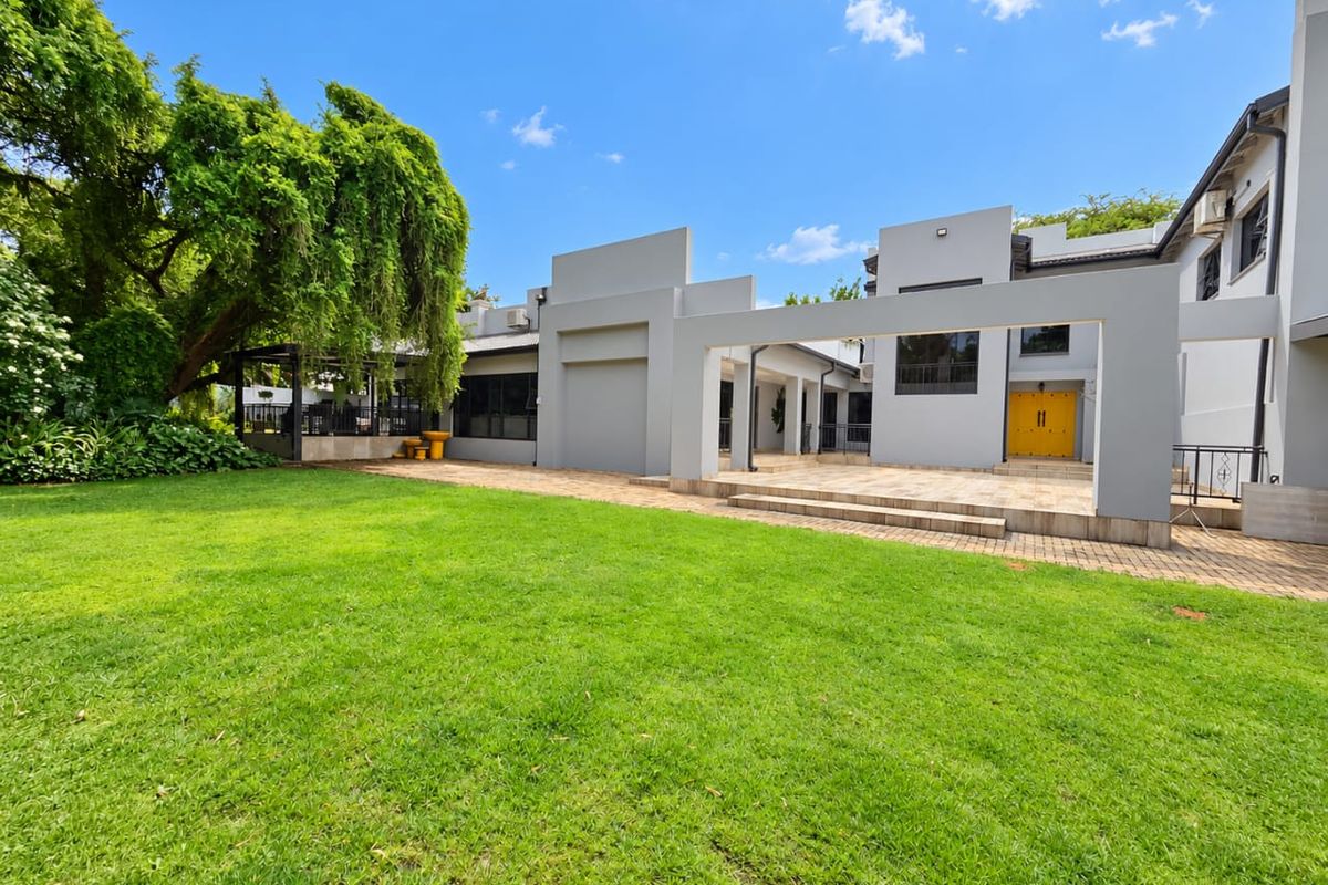 A spacious rear garden featuring a well-maintained lawn, a paved patio area, and a covered pergola structure attached to the modern home.