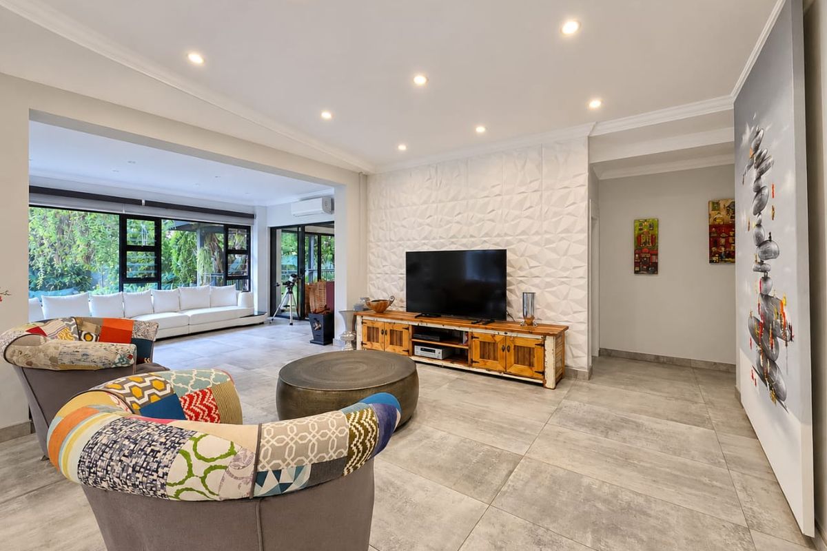 Spacious living room featuring large format floor tiles, a textured feature wall, recessed downlighting, and seamless access to the outdoor area through sliding glass doors.
