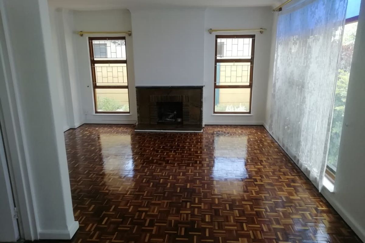 Spacious living room featuring polished parquet flooring, a central fireplace, and large windows with security bars, offering a bright and well-maintained living space.