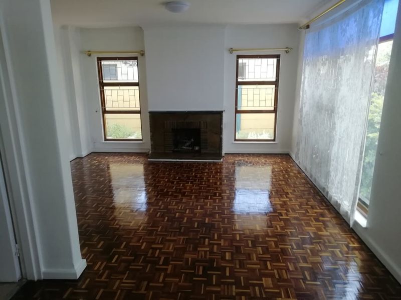 Spacious living room featuring polished parquet flooring, a central fireplace, and large windows with security bars, offering a bright and well-maintained living space.