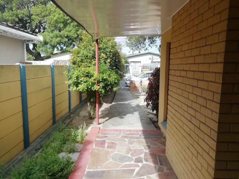 A covered outdoor walkway featuring brick wall construction, stone paving, and a precast boundary wall leading towards the property entrance.