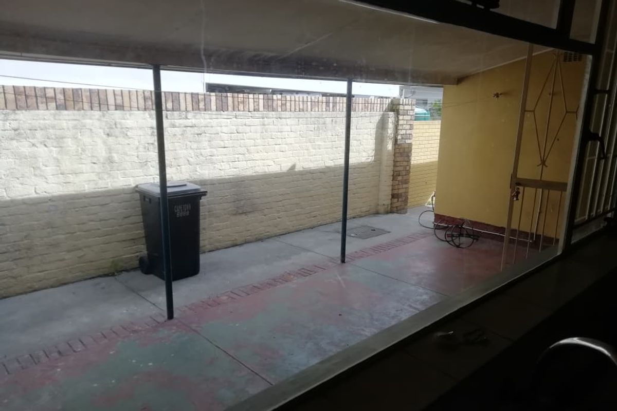 A rear exterior patio area featuring a concrete floor and brick boundary wall, viewed through a window.