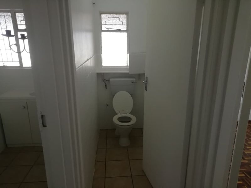A functional, dated bathroom featuring a standard toilet, tiled flooring, and a vanity cabinet, offering potential for modernization and cosmetic updates.