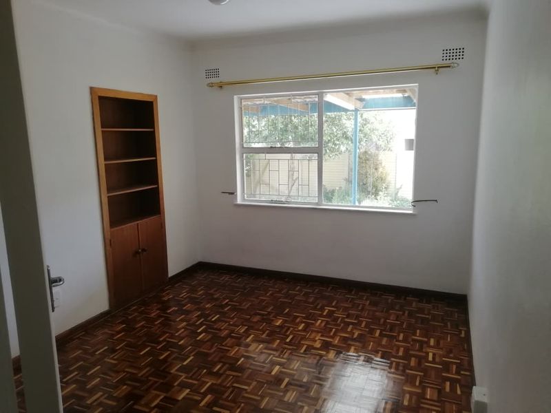 A bright, empty bedroom featuring classic parquet flooring and convenient built-in wooden shelving, offering a clean canvas for personalization.