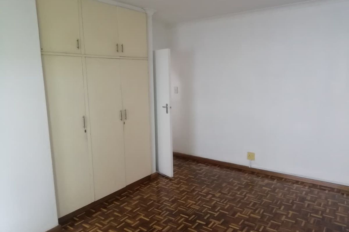 An empty bedroom featuring classic parquet flooring and built-in storage cupboards, offering a blank canvas for renovation or interior design updates.