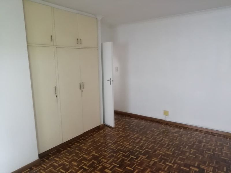 An empty bedroom featuring classic parquet flooring and built-in storage cupboards, offering a blank canvas for renovation or interior design updates.