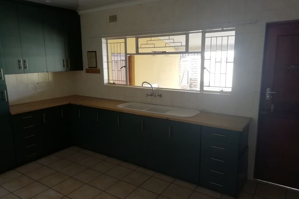 A functional kitchen featuring dark cabinetry, laminate countertops, a double basin sink, and tiled flooring, offering a clean canvas for potential updates.