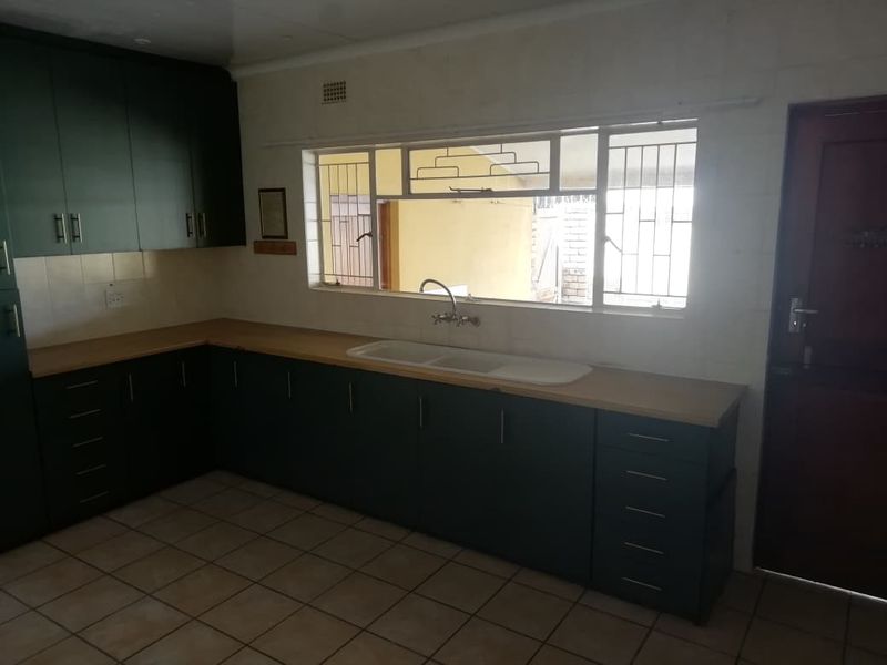 A functional kitchen featuring dark cabinetry, laminate countertops, a double basin sink, and tiled flooring, offering a clean canvas for potential updates.