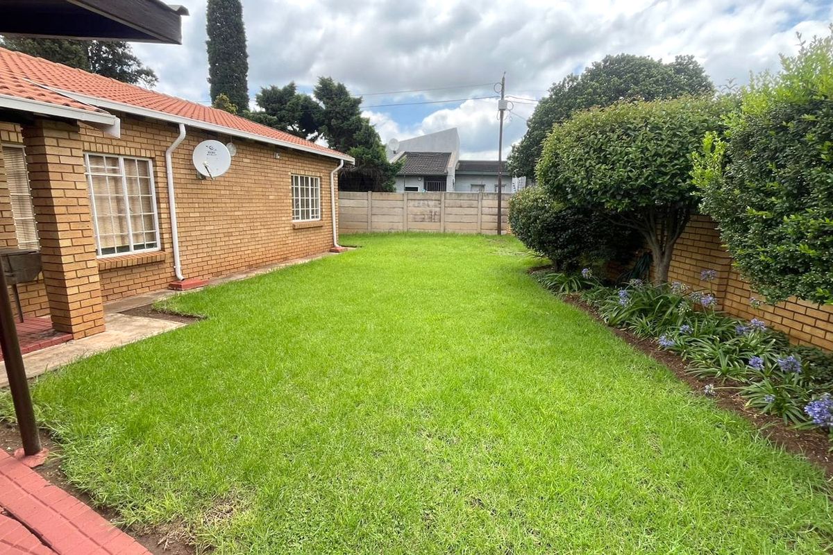 A well-maintained rear garden featuring a lush lawn, established garden beds, and a brick-faced house exterior with a covered patio area.