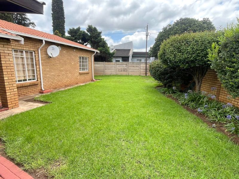 A well-maintained rear garden featuring a lush lawn, established garden beds, and a brick-faced house exterior with a covered patio area.