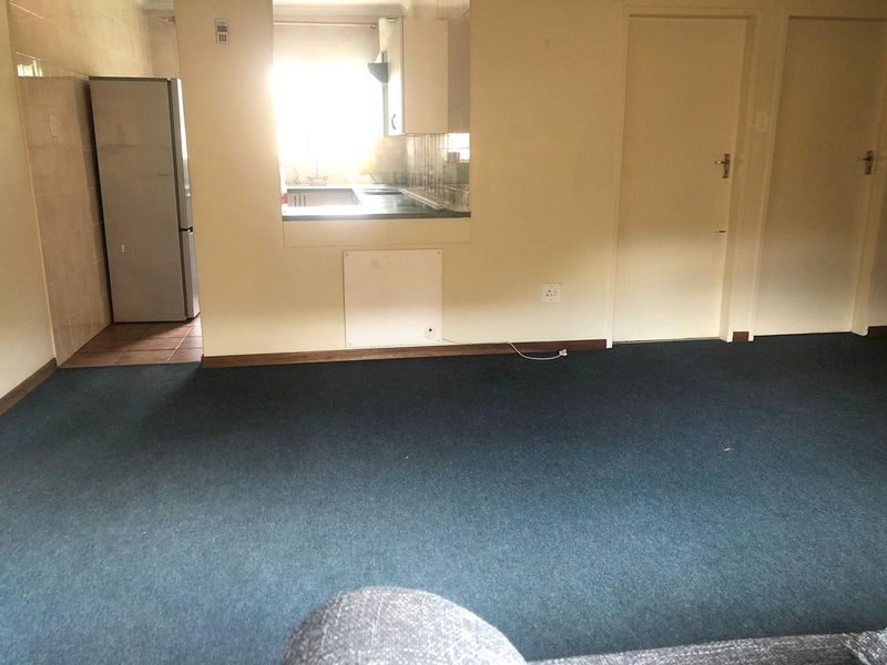 Open plan living area featuring carpeted flooring and a pass-through window to the kitchen area with built-in cabinetry.