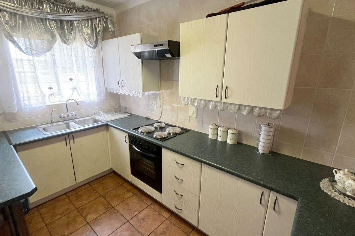 A functional kitchen featuring built-in cabinetry, laminate countertops, a double basin sink, and integrated cooking appliances with tiled splashbacks and flooring.