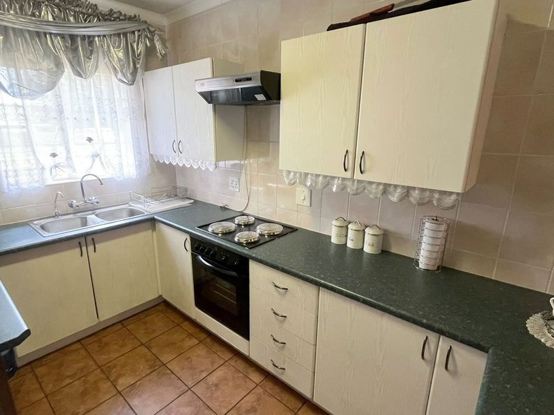 A functional kitchen featuring built-in cabinetry, laminate countertops, a double basin sink, and integrated cooking appliances with tiled splashbacks and flooring.