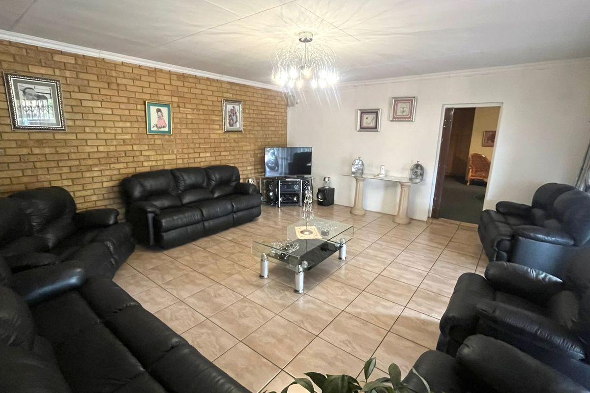 Spacious living room featuring an exposed brick feature wall, neutral ceramic floor tiles, and a central decorative light fixture.