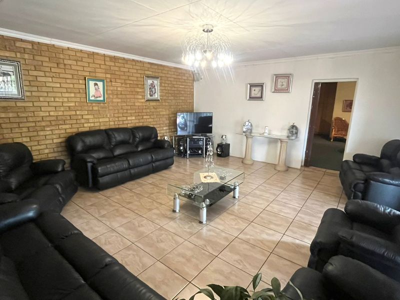 Spacious living room featuring an exposed brick feature wall, neutral ceramic floor tiles, and a central decorative light fixture.
