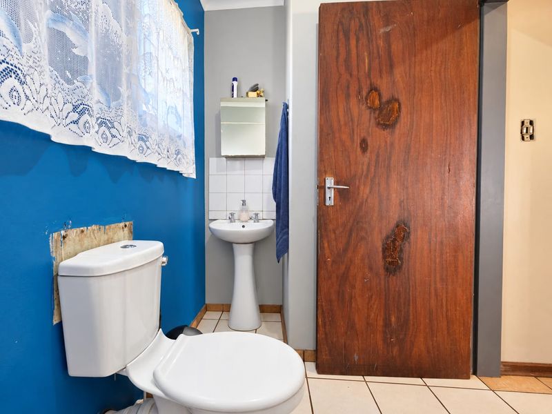 A functional bathroom featuring a pedestal basin, toilet, and tiled flooring, currently requiring cosmetic updates to the wall finishes and door.