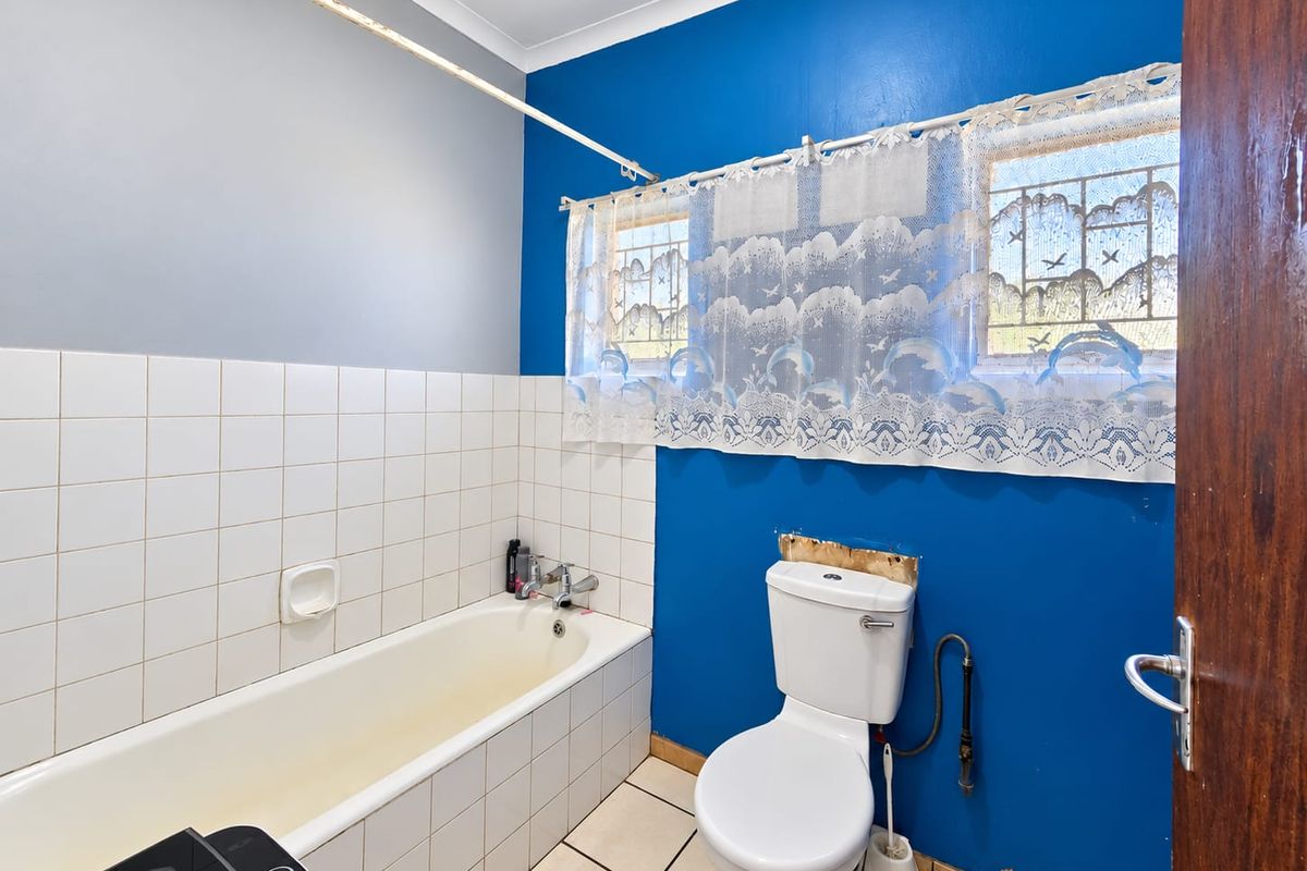 A functional bathroom featuring a bathtub, toilet, and tiled finishes, currently requiring cosmetic updates and repairs to the wall and paintwork.
