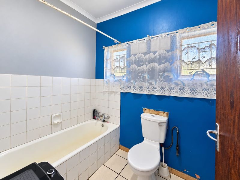 A functional bathroom featuring a bathtub, toilet, and tiled finishes, currently requiring cosmetic updates and repairs to the wall and paintwork.