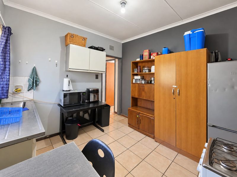 A functional kitchen area featuring tiled flooring, a stainless steel sink, and wall-mounted cabinetry, offering potential for modernization and improved layout.
