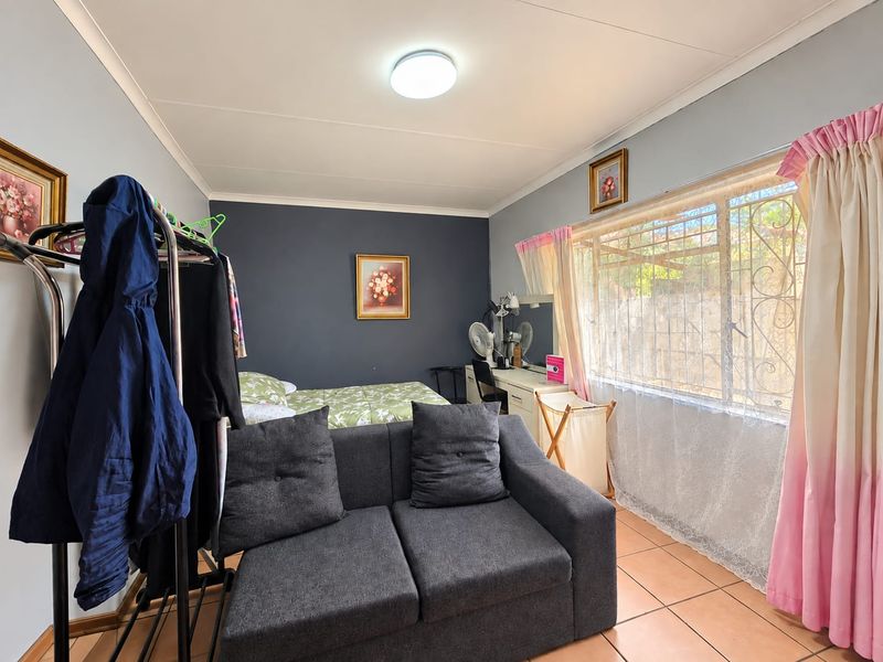 A functional bedroom featuring tiled flooring, a large window with security bars, and a neutral wall finish, offering a comfortable living space.
