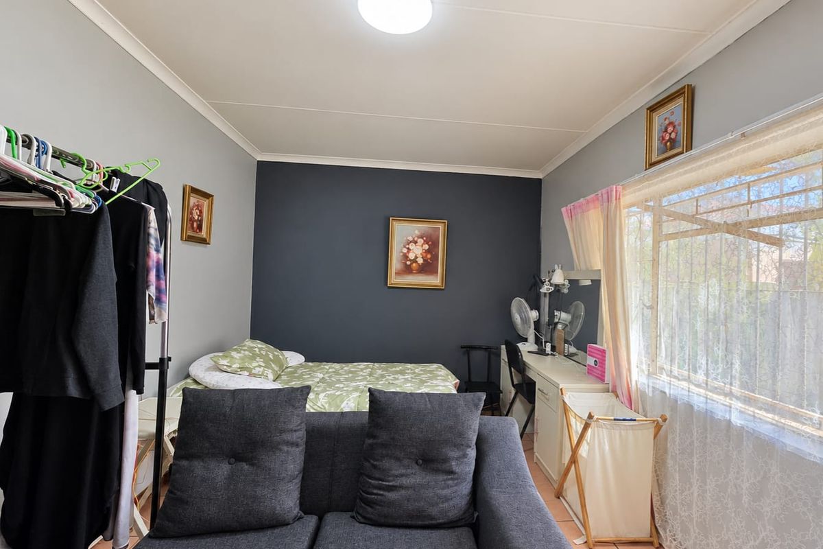 A functional bedroom featuring tiled flooring, a large window with security bars, and a neutral color palette with a dark accent wall.