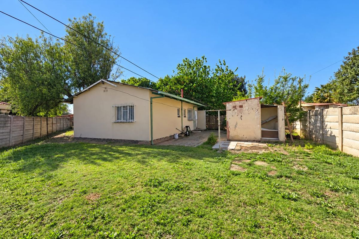 Rear view of the property featuring a spacious garden, a paved patio area, and a detached outbuilding with a precast concrete boundary wall.