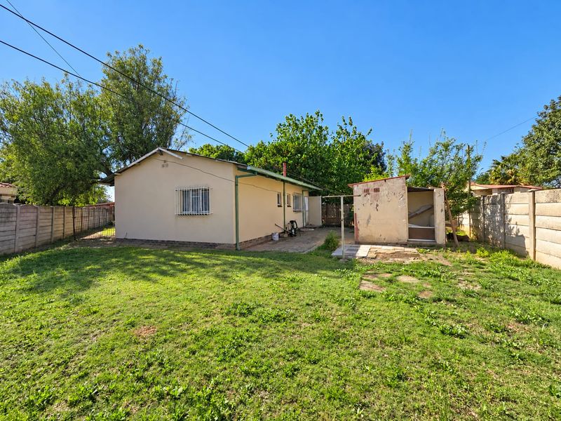 Rear view of the property featuring a spacious garden, a paved patio area, and a detached outbuilding with a precast concrete boundary wall.