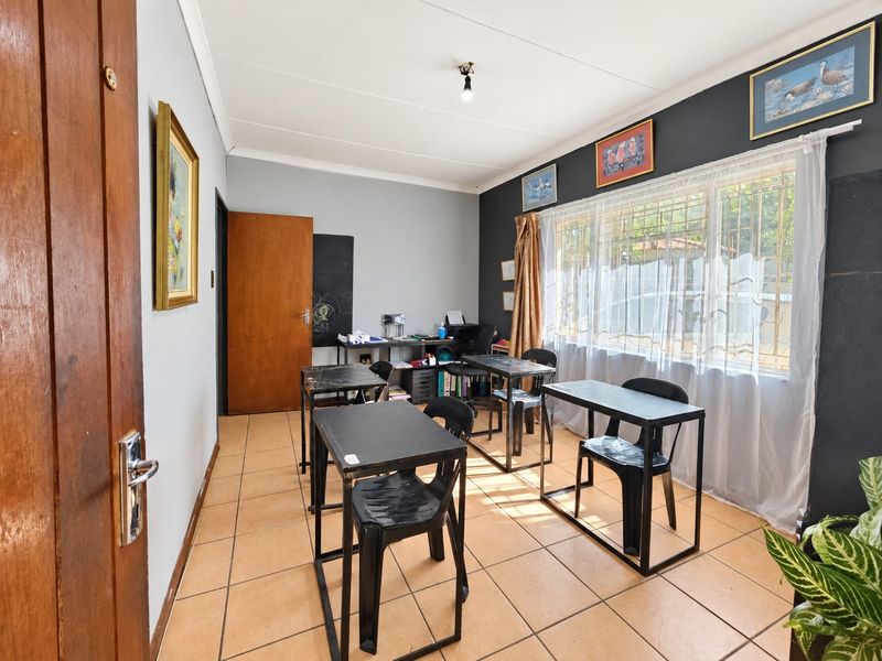 A functional office space featuring tiled flooring, a large window with security bars, and a solid wood door, suitable for a home workspace.