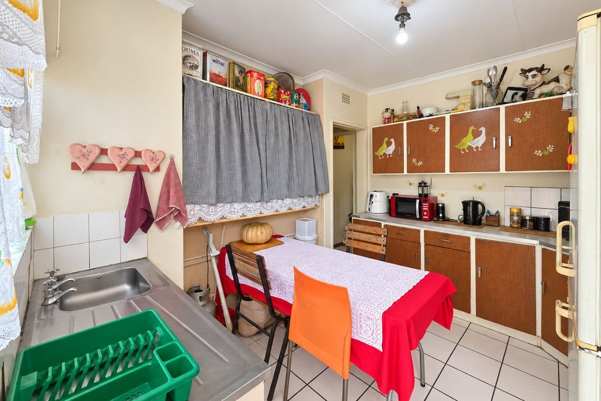 A functional kitchen featuring tiled flooring, built-in wooden cabinetry, and a stainless steel sink, offering a dated aesthetic ready for modernization.