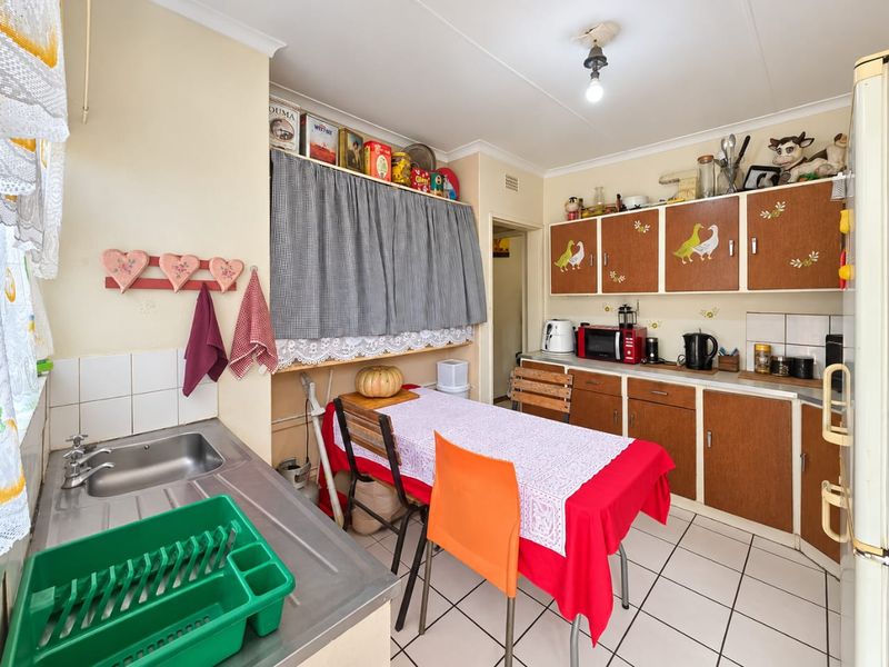 A functional kitchen featuring tiled flooring, built-in wooden cabinetry, and a stainless steel sink, offering a dated aesthetic ready for modernization.