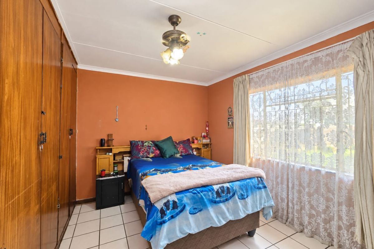 A bedroom featuring tiled flooring, built-in wooden cupboards, and a ceiling fan with integrated lighting.