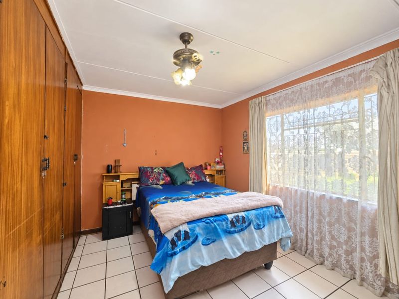 A bedroom featuring tiled flooring, built-in wooden cupboards, and a ceiling fan with integrated lighting.