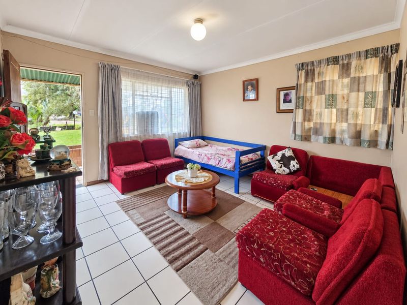 A living room featuring tiled flooring, natural light through large windows with security bars, and direct access to the outdoor area.