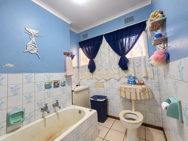 A dated bathroom featuring a built-in bathtub, wall-mounted basin, and toilet, finished with patterned ceramic wall tiles and floor tiles.