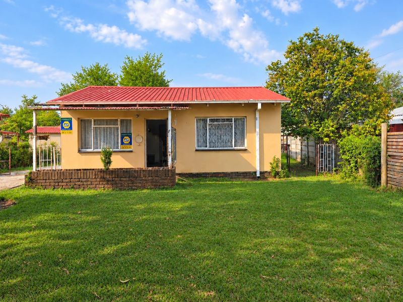 Front view of a single-story house featuring a red corrugated metal roof, brick porch, and a spacious front lawn.