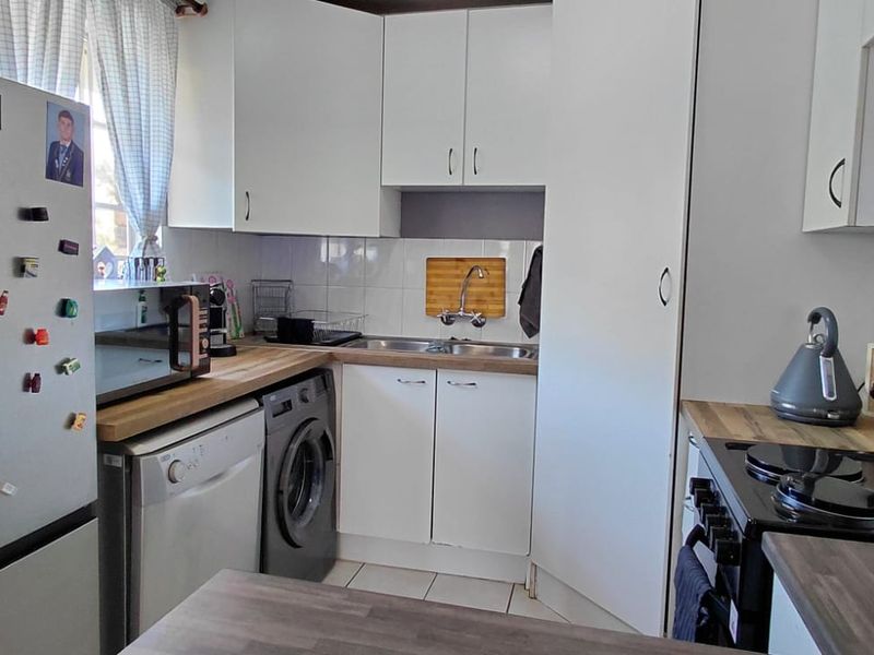 Compact kitchen featuring white cabinetry, laminate countertops, tiled backsplash, and integrated appliances, providing a functional workspace within the townhouse.