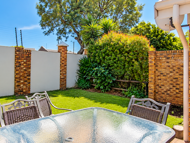 A private rear garden featuring a well-maintained lawn, brick boundary walls with electric fencing, and direct access to the home via a glass pane door.