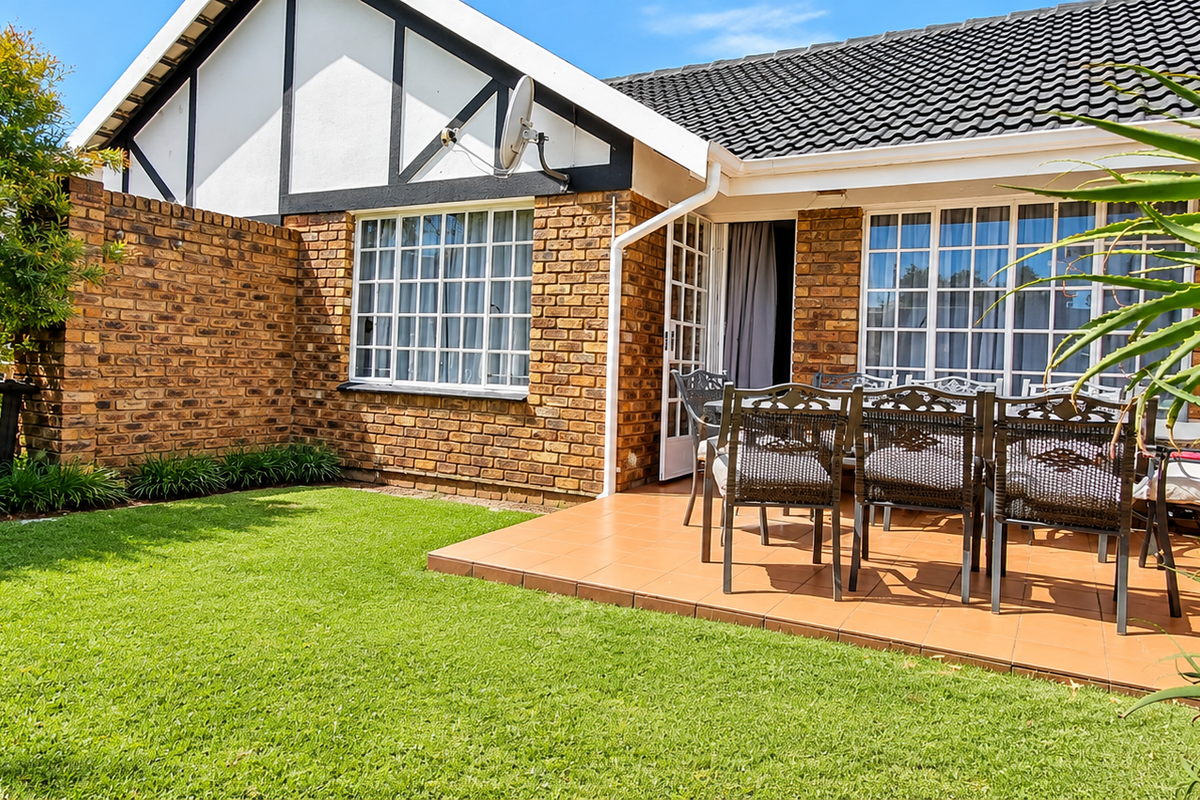 A well-maintained rear exterior view of the townhouse featuring a tiled patio area, brick facade, and a neat garden lawn.