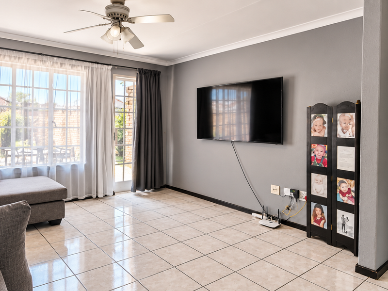 A well-maintained living room featuring neutral tiled flooring, a ceiling fan, and direct access to the outdoor area through a sliding glass door.