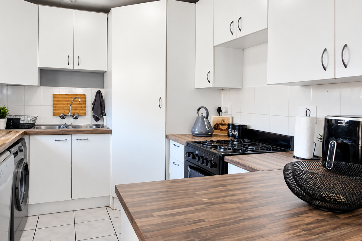 A functional kitchen featuring white cabinetry, wood-look laminate countertops, a gas hob, and a double basin sink with tiled backsplash.