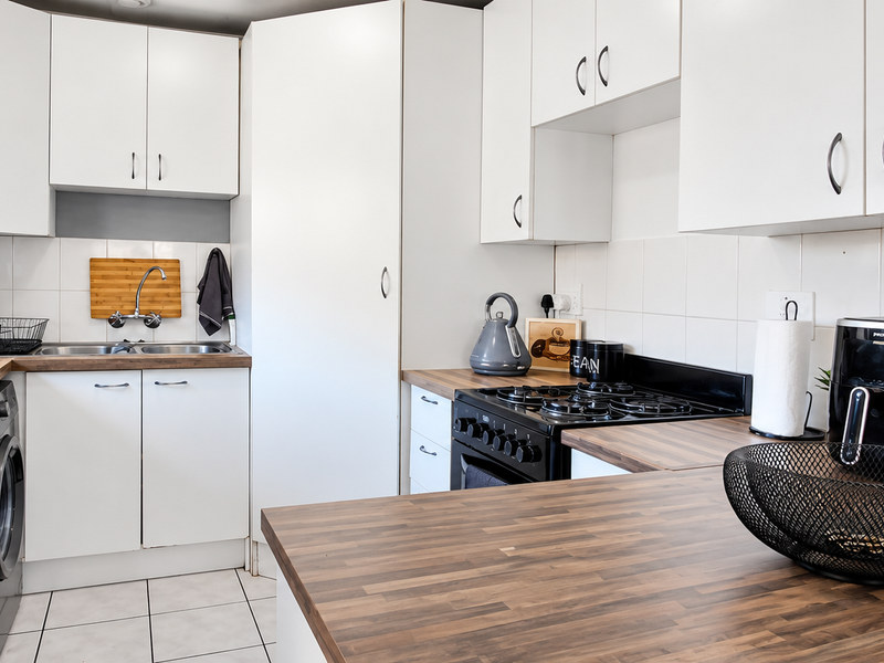 A functional kitchen featuring white cabinetry, wood-look laminate countertops, a gas hob, and a double basin sink with tiled backsplash.
