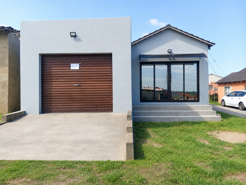 Front elevation of a modern house featuring a roller garage door, concrete driveway, and a glass-fronted entrance with concrete steps.