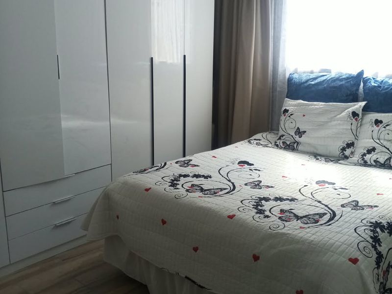 A bedroom featuring laminate flooring and a modern white built-in wardrobe with integrated drawers.