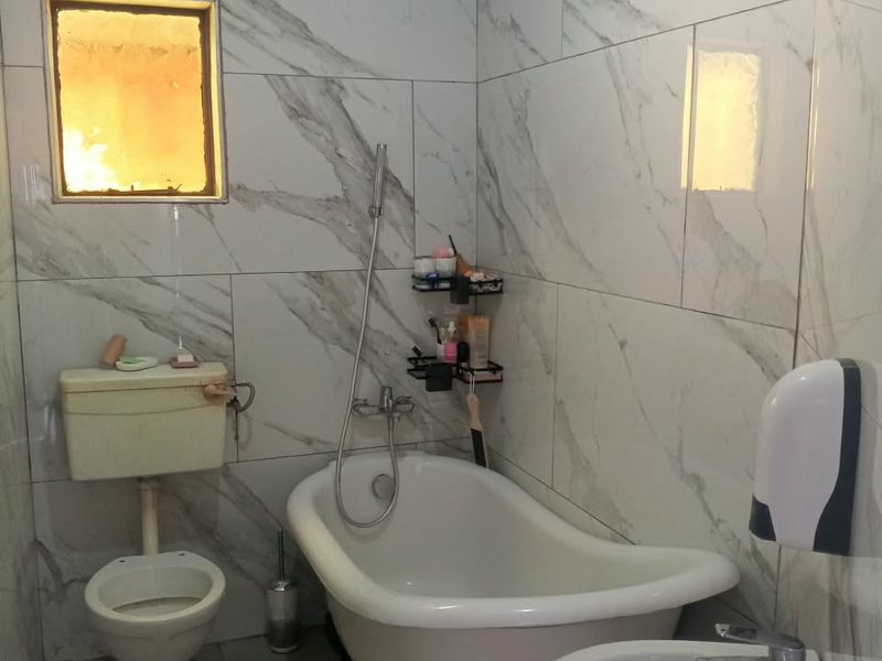 A bathroom featuring marble-look wall tiles, a freestanding bathtub with a shower handset, a pedestal basin, and a toilet.