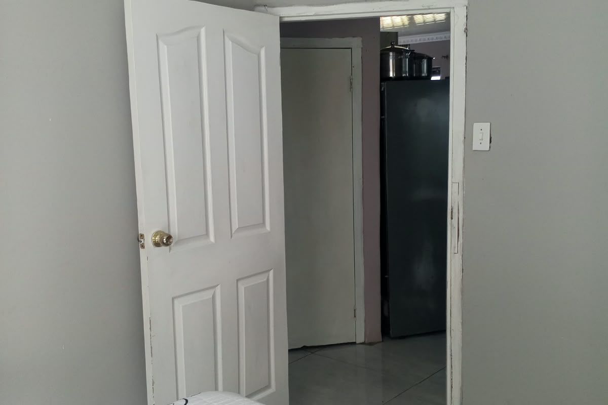 A bedroom interior featuring a panel door and visible wall cracking near the ceiling, leading into an adjacent room.