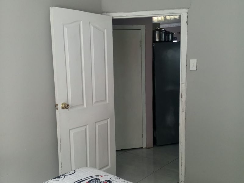 A bedroom interior featuring a panel door and visible wall cracking near the ceiling, leading into an adjacent room.