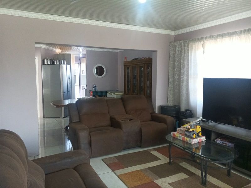 Open plan living area featuring tiled flooring and a panelled ceiling, connecting to a kitchen space.