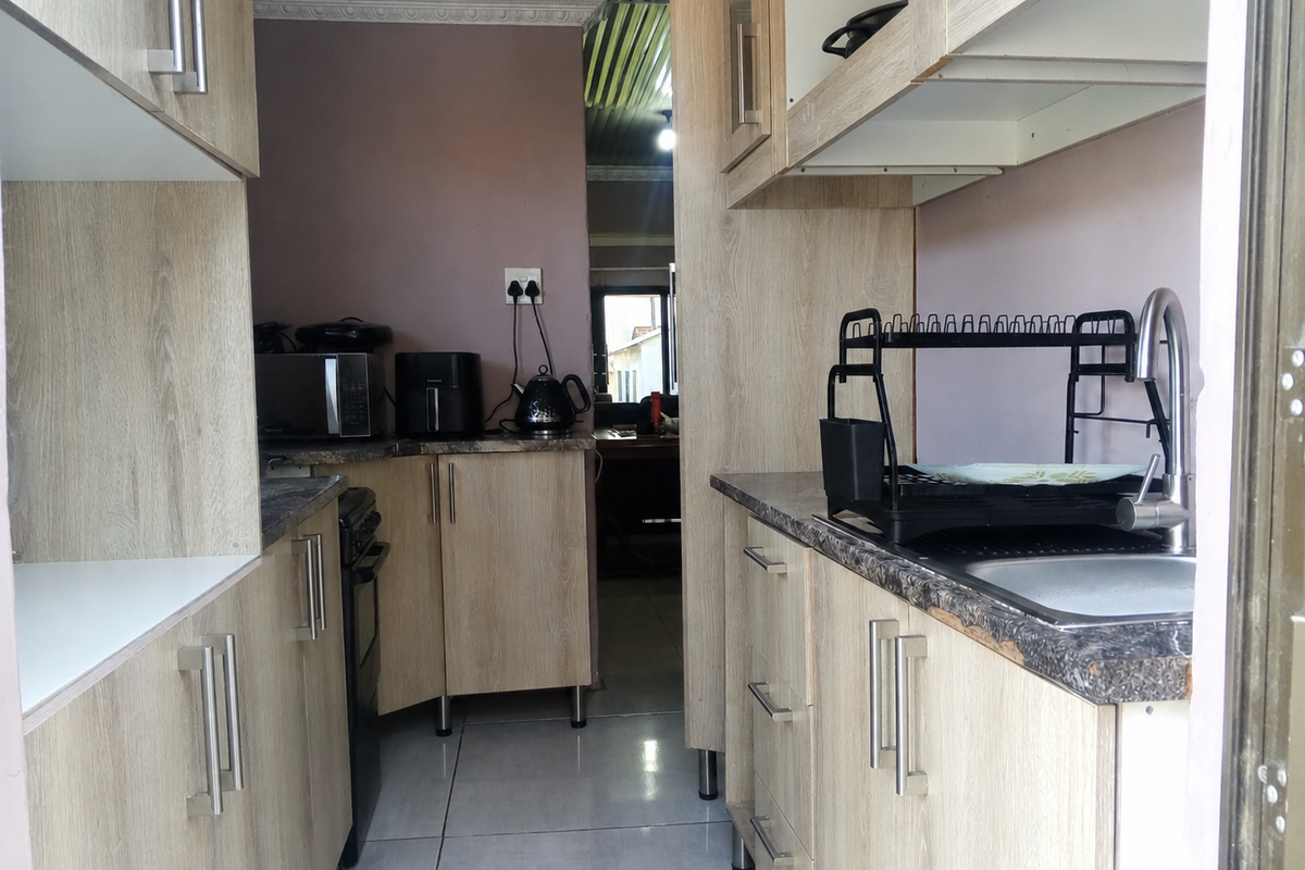 Compact galley-style kitchen featuring light wood-look cabinetry, laminate countertops, and a stainless steel sink with mixer tap.