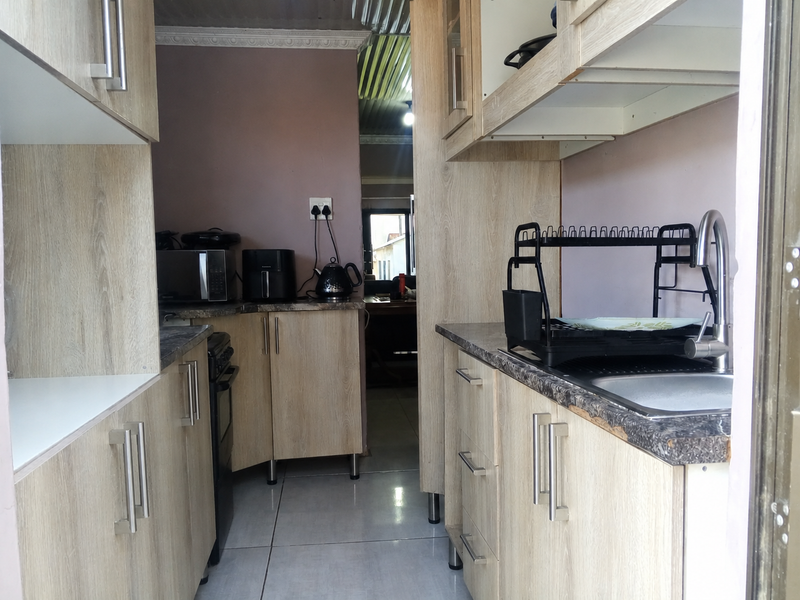 Compact galley-style kitchen featuring light wood-look cabinetry, laminate countertops, and a stainless steel sink with mixer tap.