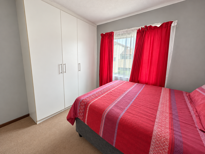 A functional bedroom featuring neutral wall tones, carpeted flooring, and a large white built-in wardrobe providing ample storage space.